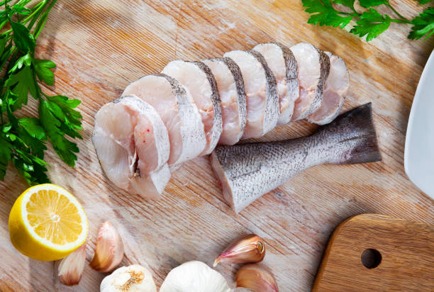 Raw hake sliced on cutting board Raw fish with condiments, pollock fillet with garlic and parsley on wooden table hake stock pictures, royalty-free photos & images