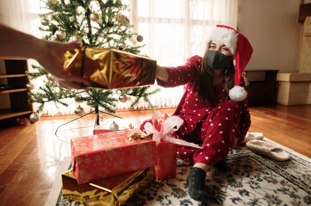 istock Young woman with face mask with presents by a Christmas tree 1282191940