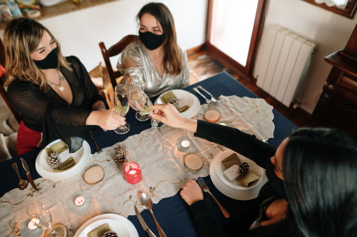Four friends having a Christmas dinner at home under COVID-19 wearing protective face masks