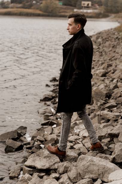 istock Confident business man walks near lake and thinks about his business during quarantine coronavirus covid-19 period. Handsome male weared formal black coat 1282198202