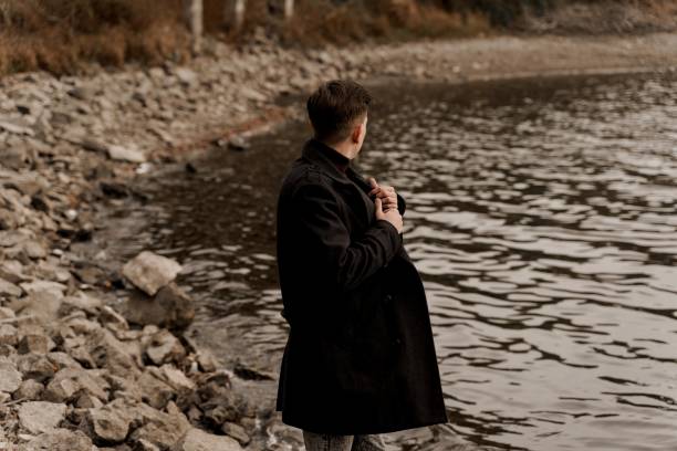 istock Confident business man walks near lake and thinks about his business during quarantine coronavirus covid-19 period. Handsome male weared formal black coat 1282198207