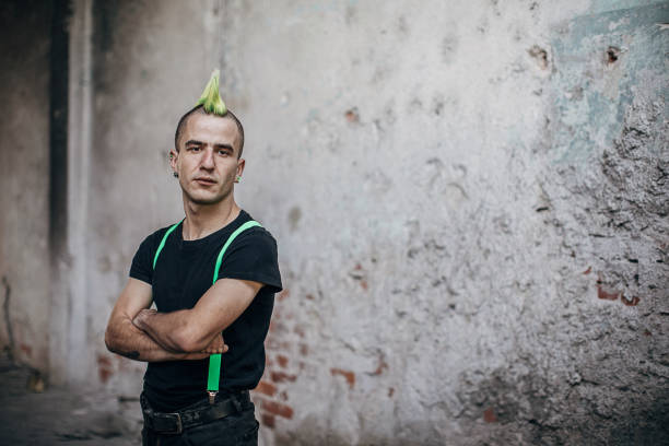 männliche punk-person steht an der wand in verlassenem gebäude - frisur irokese stock-fotos und bilder