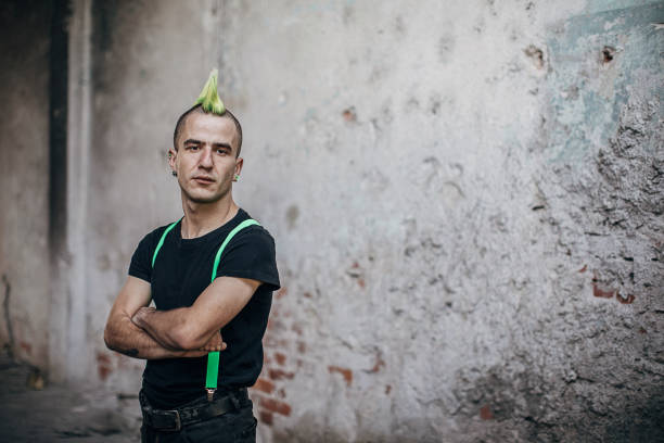 Male punk person standing by the wall in abandoned building Male punk person with yellow Mohawk hairstyle, standing by the wall in abandoned building with arms crossed. mohawk stock pictures, royalty-free photos & images