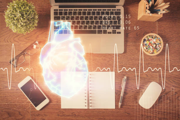 istock Heart hologram drawings over computer on the desktop background. Top view. Multi exposure. Concept of medical education. 1282203032
