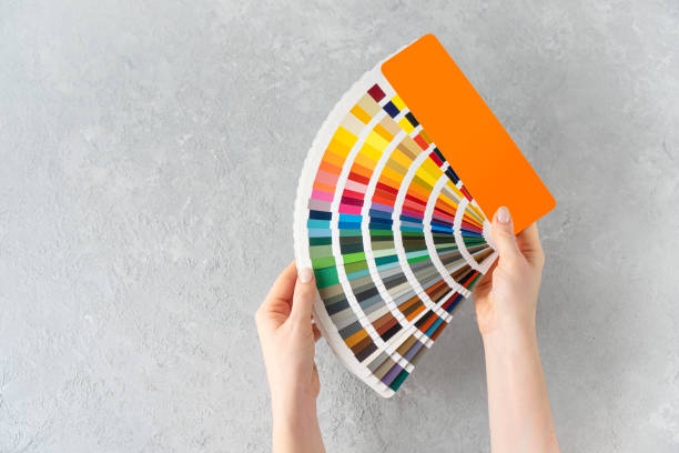 What color to paint the walls concept. Female hands holding a ral colors palette fan on a concrete background. Copy space. stock photo
