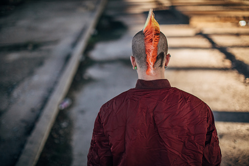 Male punk person with yellow Mohawk hairstyle, standing in abandoned building alone.