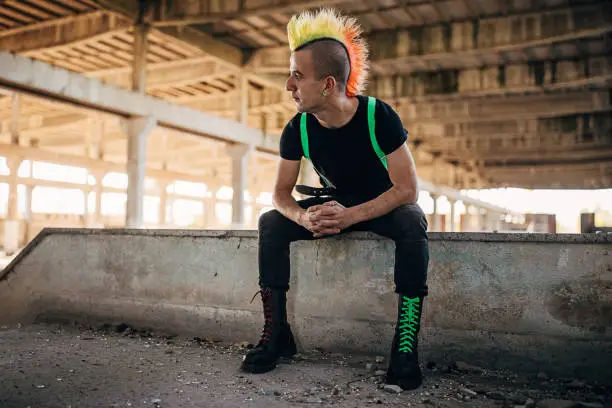 One young male punker with colorful coiffure sitting in abandoned building.