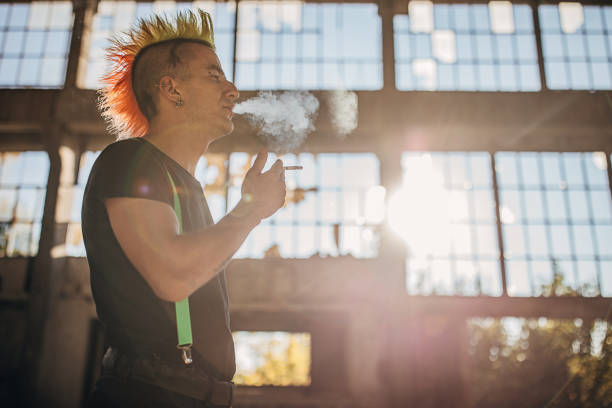 istock Panker with colorful coiffure standing in abandoned warehouse and smoking cigarettes 1282206328