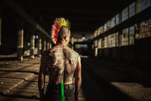 Rear view of one young shirtless panker with tattoos on back One young male shirtless punker with tattoos on back and colorful coiffure standing in abandoned warehouse, rear view. body adornment rear view young men men stock pictures, royalty-free photos & images