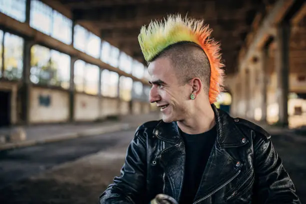 One young male punker with colorful coiffure sitting in abandoned warehouse and drinking beer.