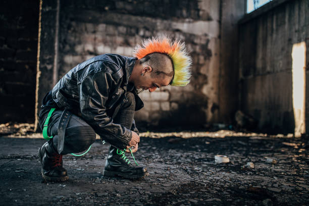 One young male punker with colorful coiffure kneeling in abandoned warehouse and tying a shoelace.