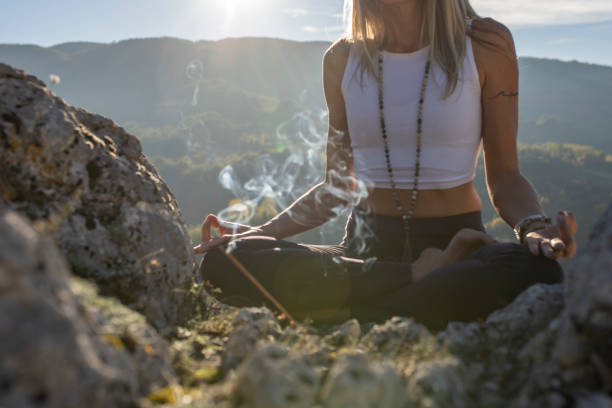 Spiritual moment of a woman meditating on the top of cliff Close up shot of fit woman meditating in nature barefoot with sun rays suhining from her background. mantra stock pictures, royalty-free photos & images