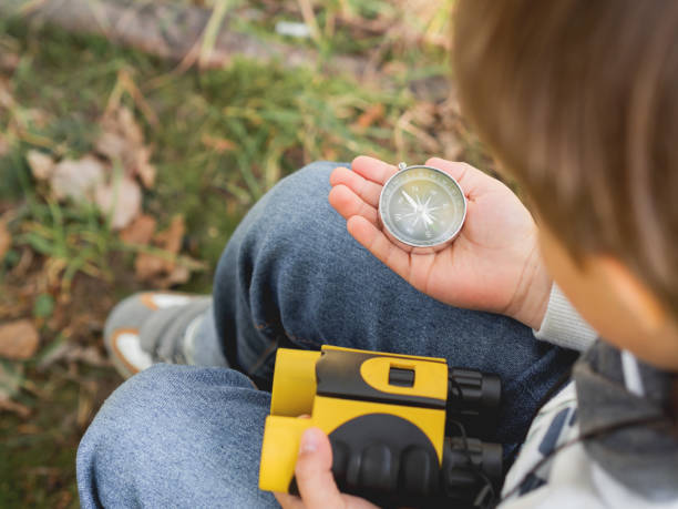 istock Little explorer on hike in forest. Boy with binoculars and compass sits on stump and reads map. Outdoor leisure activity for children. Summer journey for young tourist. 1282214227