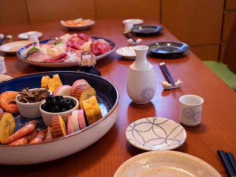 The table being set for a traditional new year's dinner in Japan, with sashimi, osuimono and sake