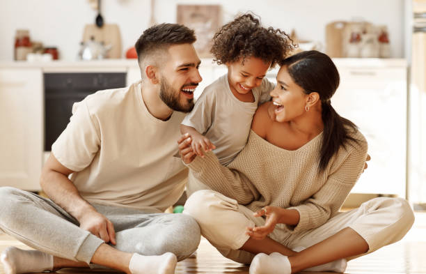feliz familia multiétnica mamá, papá y niño riendo, jugando y cosquillas en el suelo en la cocina acogedora en casa - relajación fotos fotografías e imágenes de stock