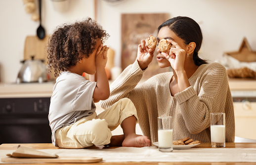 happy african american family: mother and little son eat cookies with milk for breakfast at home