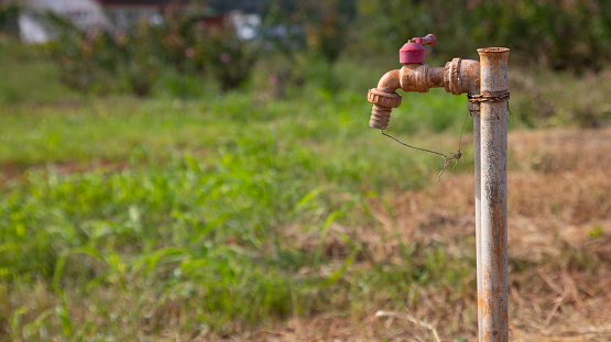 Selective focus with blurred background of grunge and rusty faucet installed in the field of remote rural area for people living and agriculture shows problem of water shortage and global warming.