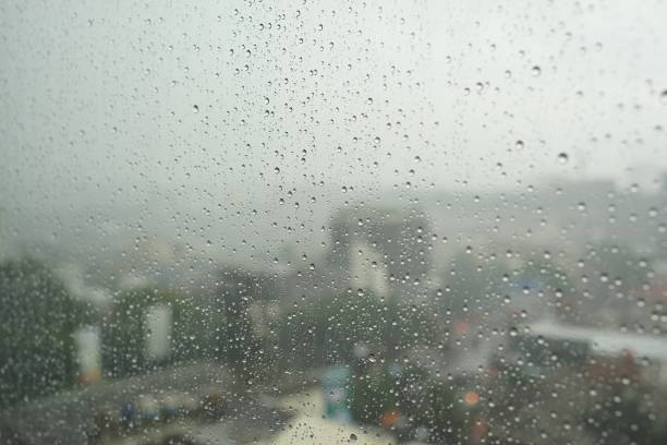 istock Water drop on glass window with cloudy sky and city on background 1282235911