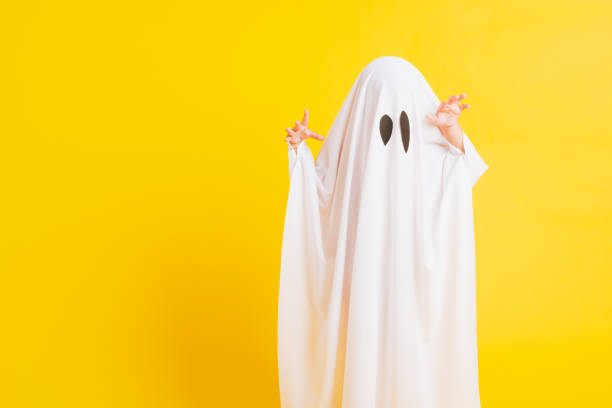Funny Halloween Kid Concept, Closeup a little cute child with white dressed costume halloween ghost scary, studio shot isolated on yellow background