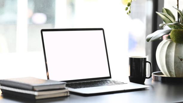 istock Minimal workplace with blank screen laptop, coffee cup and note books on white desk. 1282237116