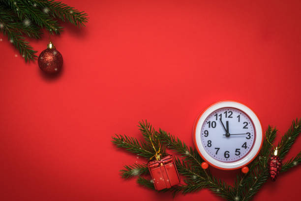 istock Red and white alarm clock, spruce branches and decorations on a red background. 1282239480