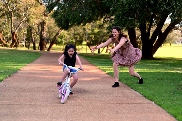 Mother screaming while her daughter riding a bike loosing balance Young mother screaming while her daughter riding a bike  without wearing a helmet loosing balance on a path of a city park. protective sportswear stock pictures, royalty-free photos & images