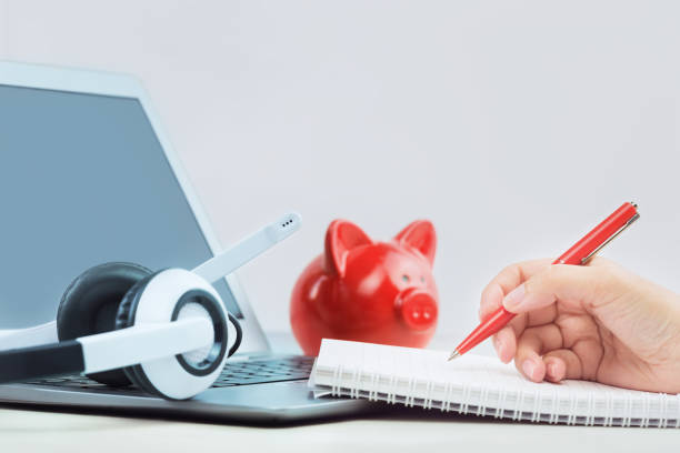istock Laptop with headphones, coins bank and note pad on white desk 1282244607