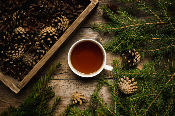 Christmas hygge background with cup of tea, pine branches and crate of cones on the wooden background Christmas hygge background with cup of tea, pine branches and crate of cones on the wooden background. Selective focus. Shallow depth of field. pine needle tea stock pictures, royalty-free photos & images