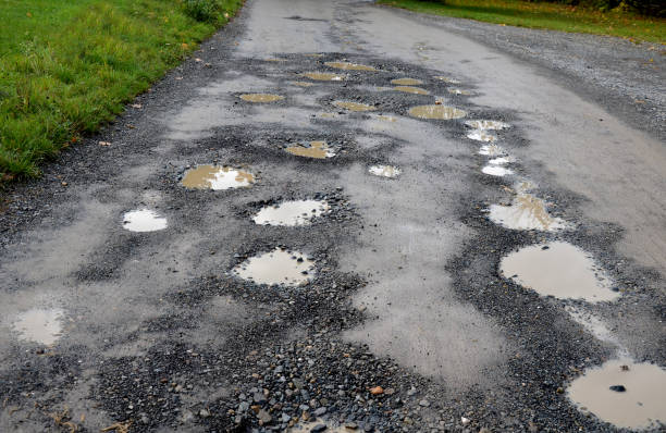 parking près des nids-de-poule qui sont sur le chemin de terre. lavage de voiture garé à nouveau est sale de l’eau brune avec de la boue. la limousine verte a de la peinture sale. le conducteur téméraire passe par les flaques d’eau trop vite. domm - irrégulier photos et images de collection