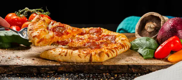 Delicious cooked Pepperoni Pizza with fresh ingredients on a timber board, food background.