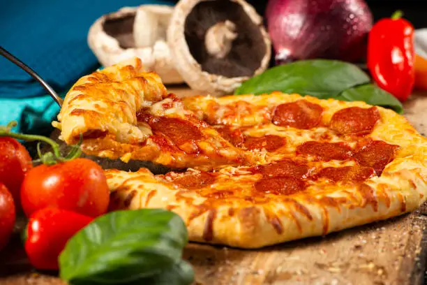 Delicious cooked Pepperoni Pizza with fresh ingredients on a timber board, food background.