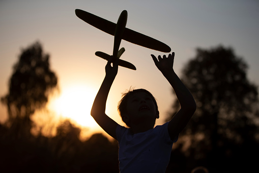 Happy child plays with an airplane at sunset. Silhouette of a boy with an airplane on the background of the sun.