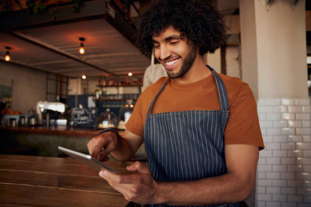 istock Happy young man waiter wearing apron holding and using digital tablet in cafe 1282265449