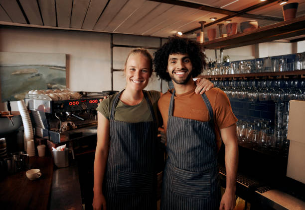 istock Young cafe owners wearing apron standing behind counter in cafe looking at camera 1282265592