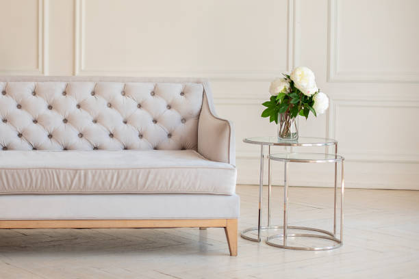istock Modern Spacious minimalistic living room interior with a gray sofa and a coffee table with a vase with a bouquet of peonies flowers against a white wall. Scandinavian  interior home. Cozy room decor. 1282268508
