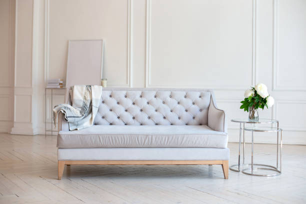 istock Modern Spacious minimalistic living room interior with a gray sofa and a coffee table with a vase with a bouquet of peonies flowers against a white wall. Scandinavian  interior home. Cozy room decor. 1282268510