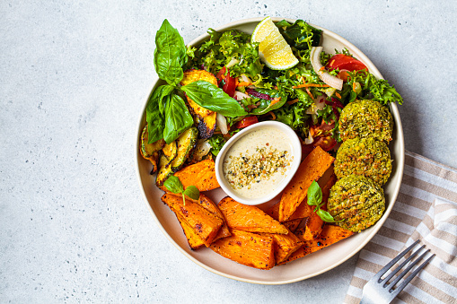 Falafel salad bowl. Vegan lunch plate - baked chickpea cutlets with baked sweet potatoes and vegetable salad in a white plate.