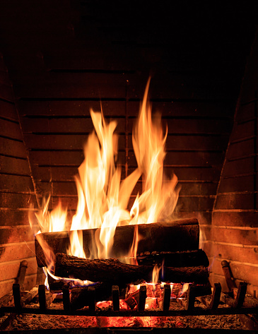 Burning fireplace. Cozy warm home, christmas time. Wood logs fire glowing in the dark. Vertical closeup view