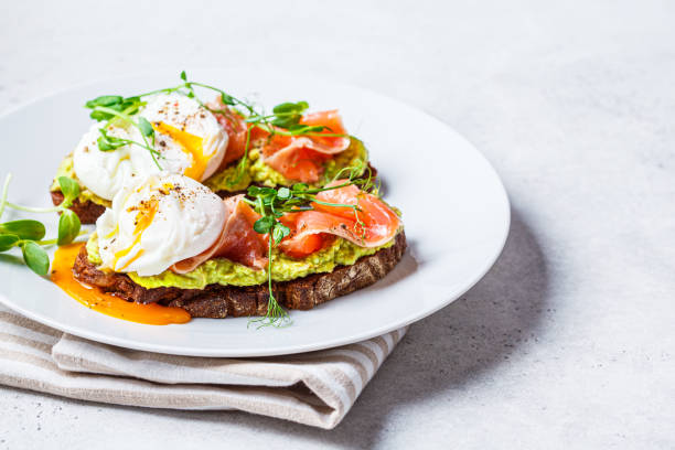 istock Toast with salmon, poached egg and avocado on white plate. Poached egg with salmon and guacamole on rye bread. 1282269820