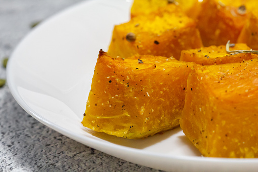 Baked pumpkin in a white plate. Side view. Pumpkin cooked in the oven. Cut pieces of pumpkin.A traditional autumn dish of baked pumpkin. Macro photography of food.