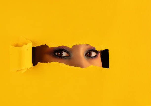 istock Girl with makeup looks through a torn hole in paper. 1282276987