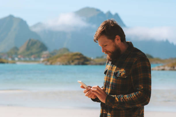 istock Man using smartphone walking on beach modern technology influencer freelancer lifestyle summer vacations outdoor sea and mountains landscape in Norway 1282277297