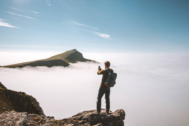 Man blogger with smartphone on mountain cliff travel vacations adventure content creator influencer lifestyle outdoor over clouds landscape in Norway