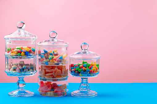 Glass containers with candies and sweets against pink background