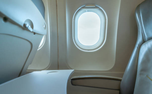 istock Plane window with white sunlight. Empty plastic airplane tray table at seat back. Economy class airplane window. Inside of commercial airline. Seat with armchair. Leather seat of economy class plane. 1282279820