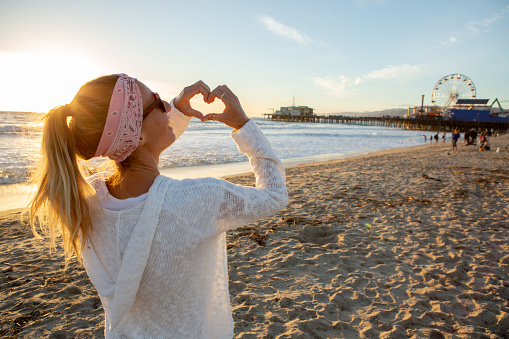 Girl making a heart shape finger frame with hands on Santa Monica Beach, California, USA