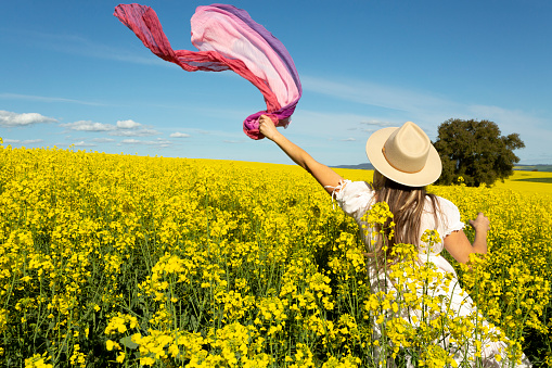 Woman in white sun dress in a field of flowering golden canola