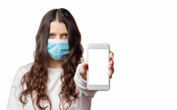istock Covid-19. Girl in a protective mask shows a smartphone with a blank screen on a white background. Pandemic of coronavirus. Epidemic of nCoV. 1282284678