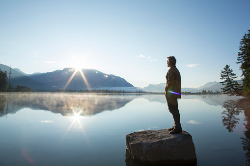 Hombre maduro se para en la roca, en el lago, y mira el amanecer photo