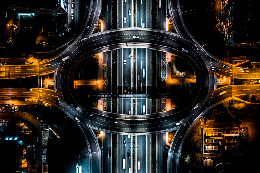 The overpass circle road and highway below it with yellow and white street lights during the night in a city seen directly from above.